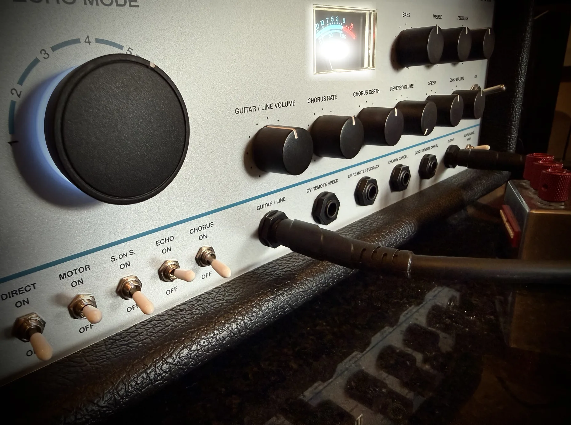 A tape echo's control panel under raking light — mode knob, level meter, switch row and patch field in close-up.