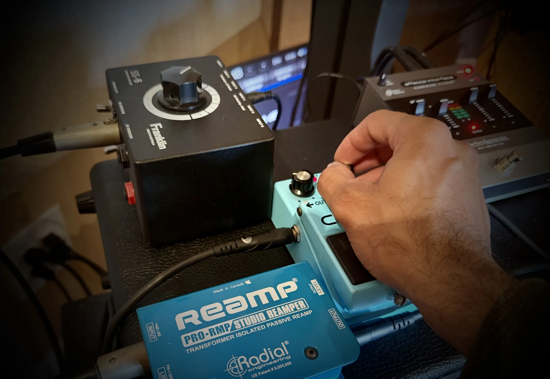 A hand setting a pedal on the bench, wired through a passive reamp box and a splitter for measurement.